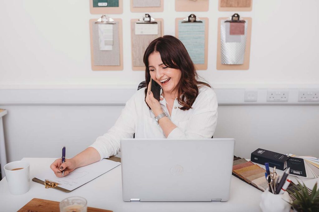 female interior designer on the phone in her office with laptop and notebook and material and paint swatches