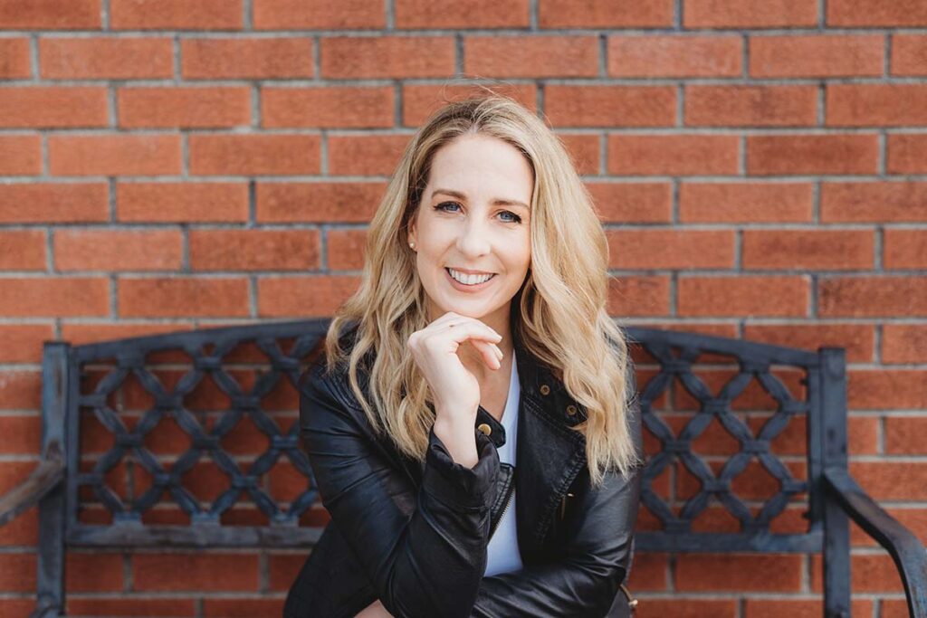 female headshot sitting on bench in front of red brick wall