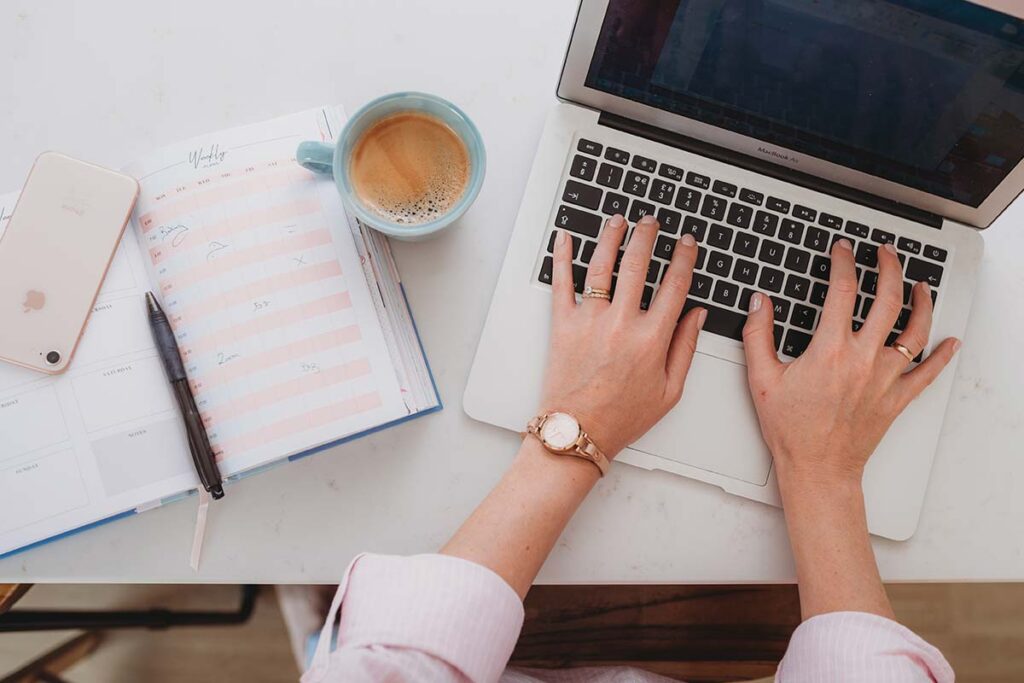 woman hands typing on laptop with coffee cup, iPhone and journal to the side