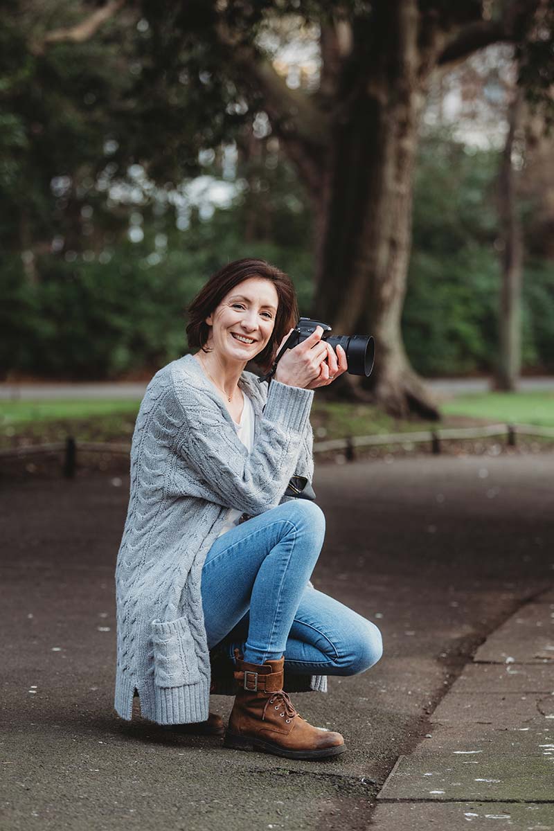 woman kneeling down smiling at camera with camera in her hand