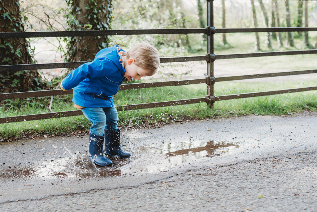 Child in rain boots splashing through puddles during a relaxed outdoor shoot