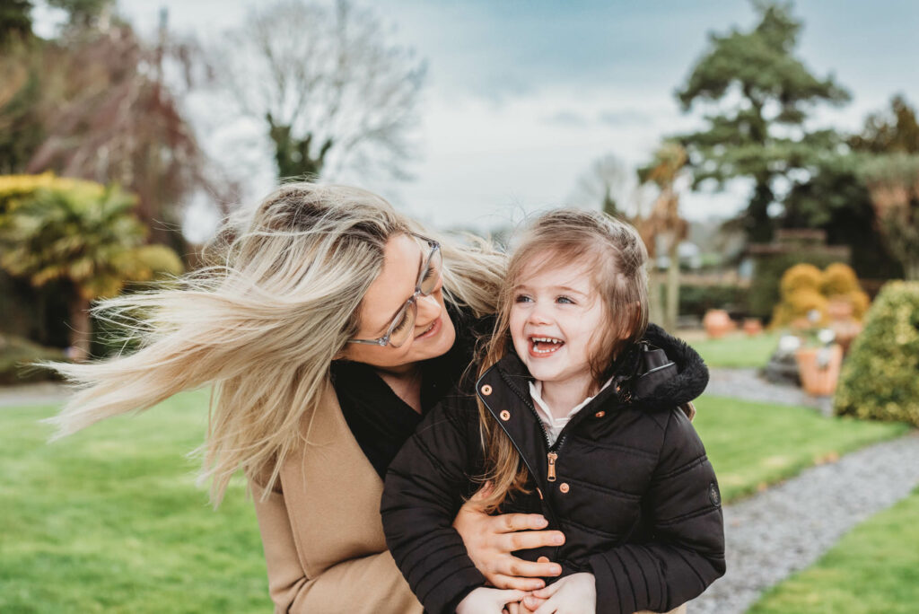 Mother and daughter wearing warm coats cuddling outside to keep warm during outdoor winter photo session in Offaly.