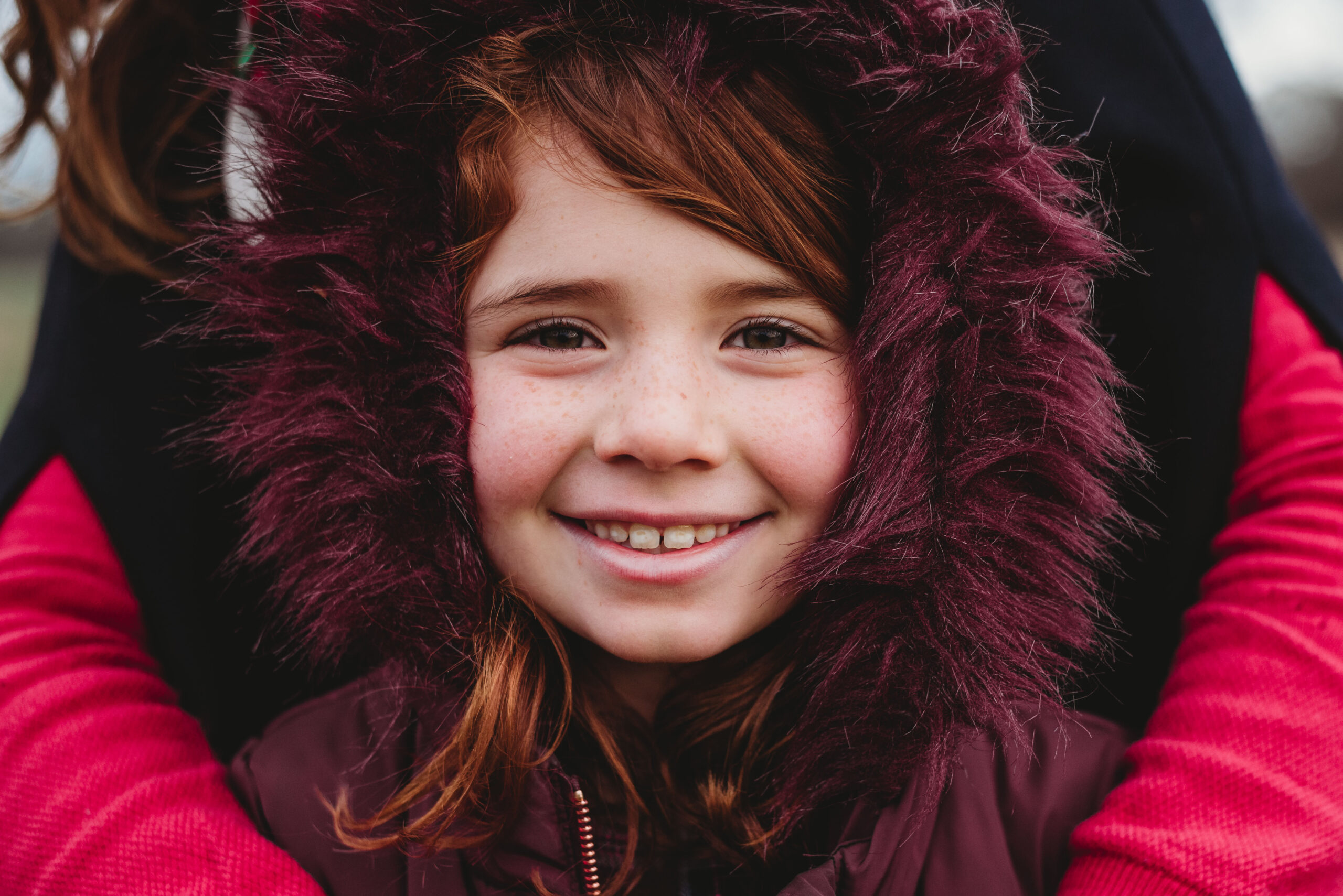 Child wearing cosy winter coat with fur trim during family photoshoot.